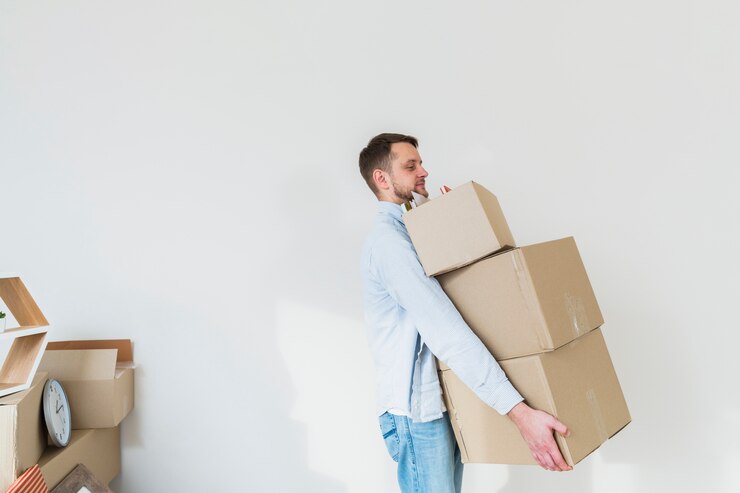 Free Photo side view of a young man carrying the stack of cardboard boxes against white wall