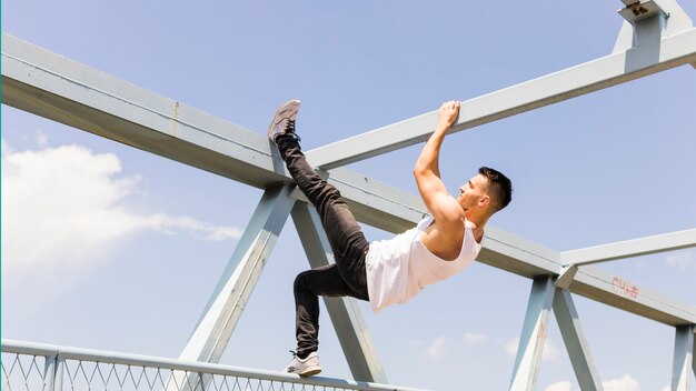 Side view of a young man climbing on the ceiling of a bridge