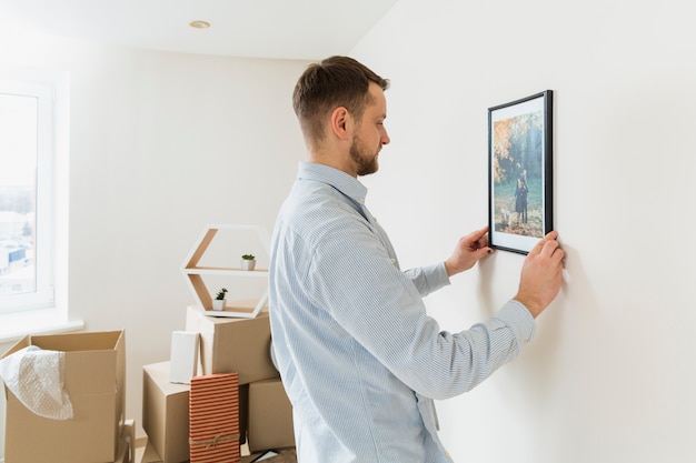 Side view of a young man fixing the picture frame on wall at new home