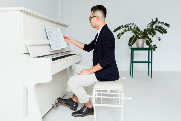 Side view of a young man sitting in front of piano reading the musical sheet