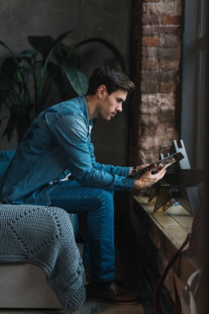 Side view of young man sitting on sofa reading book