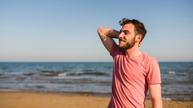 Side view of a young man standing at beach against blue sky