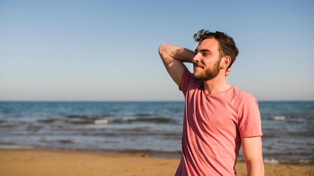 青い空を背景にビーチに立っている若い男の側面図