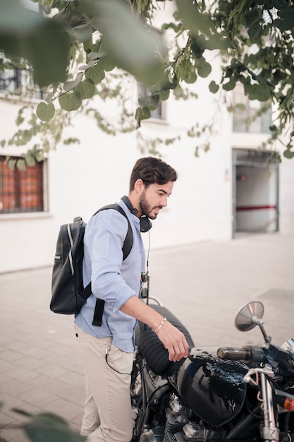 Side view of a young man standing with his motorbike