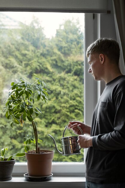 Вид сбоку молодой человек поливает растение