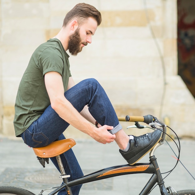 Foto gratuita vista laterale di un giovane uomo con la bicicletta piegando i suoi jeans