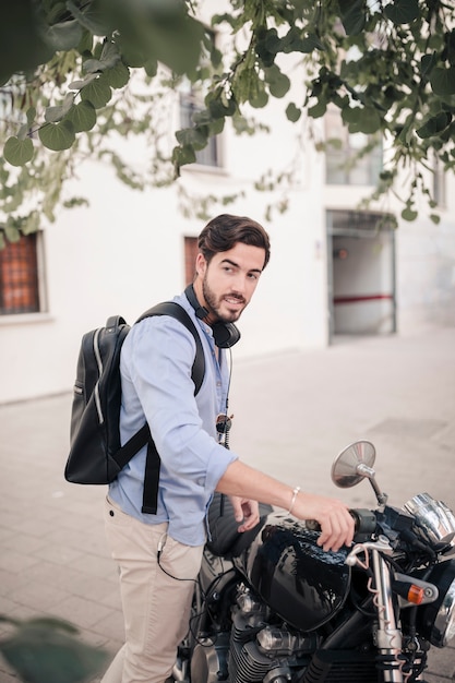 Боковой вид молодого человека с его мотоциклом