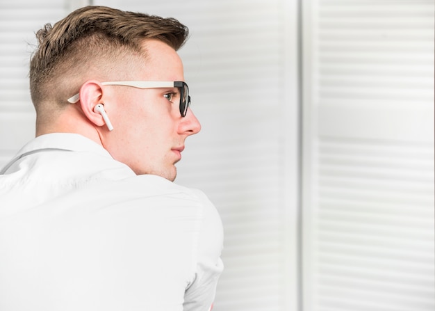 Free photo side view of a young man with white wireless earphone wearing eyeglasses looking away