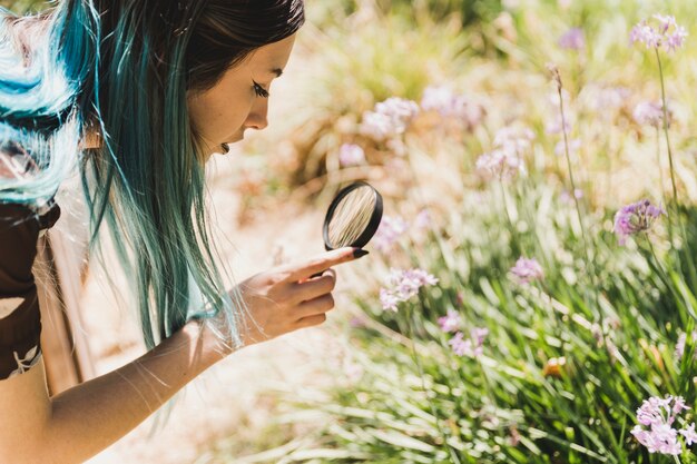 Side view of a young modern woman looking at flowers through magnifying glass