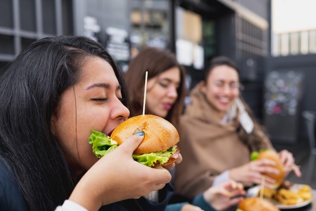 ハンバーガー​を​噛んでいる​若い​女性​の​側面図​。​レストラン​の​テーブル​に​座っている​女性​。