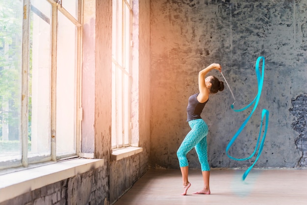 Side view of a young woman dancing with blue ribbon