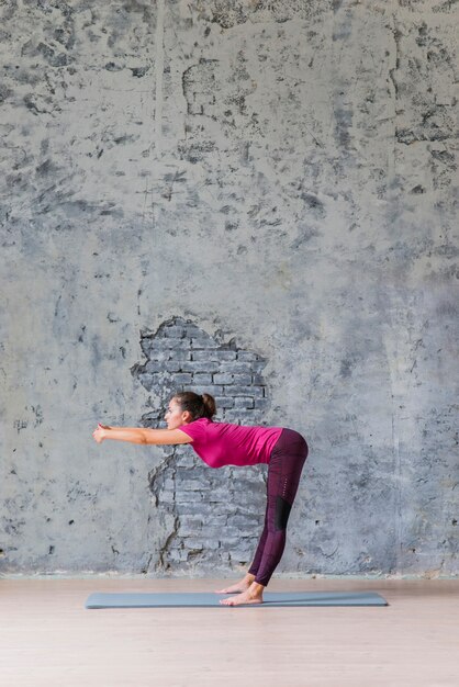 Side view of young woman doing stretching exercise against grey background