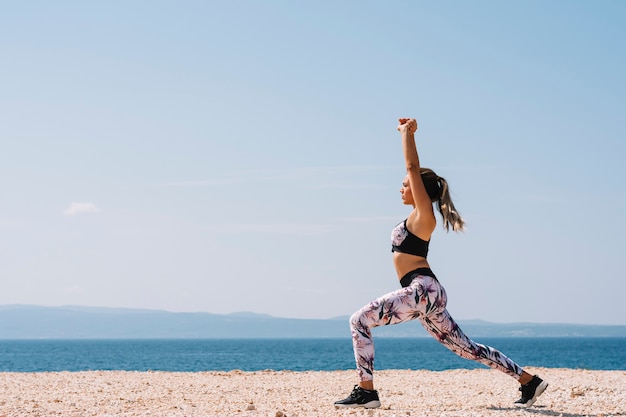 Vista laterale di una giovane donna che fa esercizio di stretching vicino alla spiaggia
