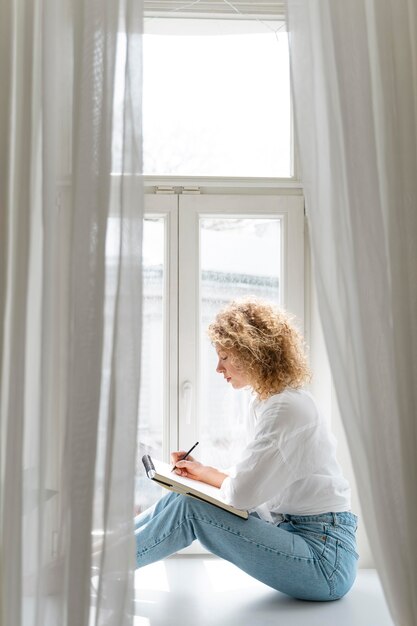 Side view of a young woman drawing at home near the window