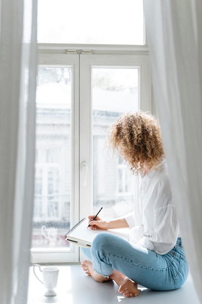 Side view of a young woman drawing at home near the window