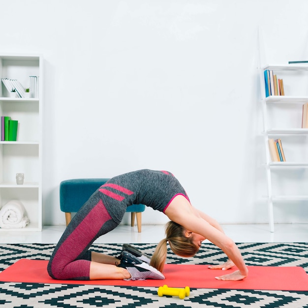 Side view of young woman exercising on red exercise mat over the pattern carpet at home