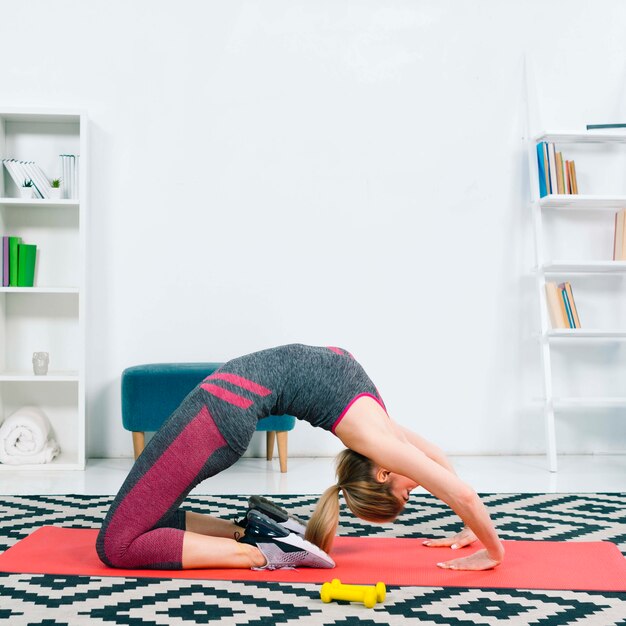 Side view of young woman exercising on red exercise mat over the pattern carpet at home