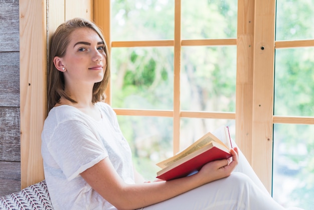 Vista laterale del libro della tenuta della giovane donna che esamina macchina fotografica