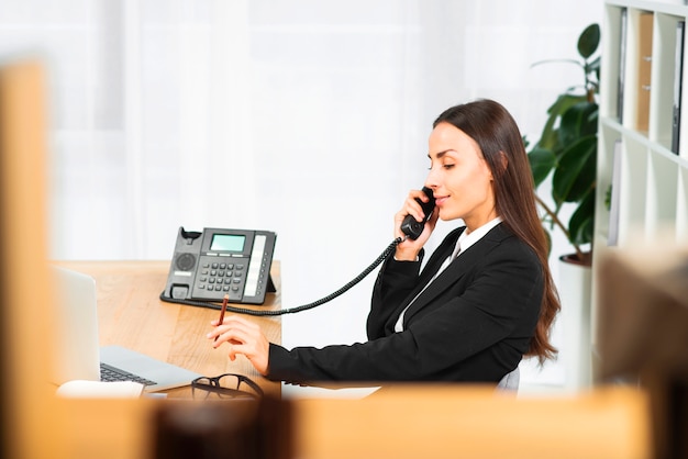 Side view of a young woman holding pencil in hand talking on telephone