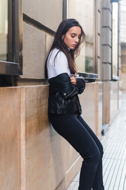 Side view of a young woman leaning on wall by the sidewalk
