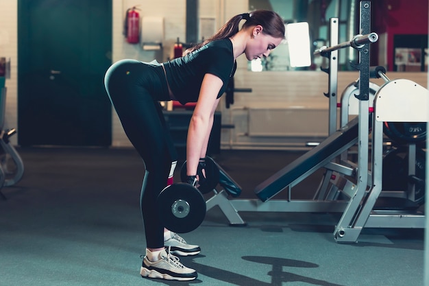 Side view of a young woman lifting weight in fitness center