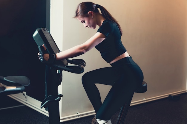Side view of a young woman riding an exercise bike