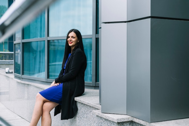 Side view of a young woman sitting outside building looking at camera