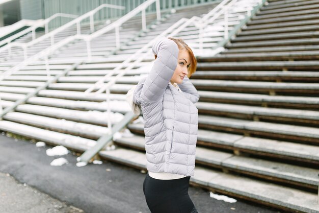 Side view of a young woman standing in front of bleachers