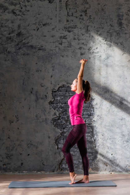 Вид сбоку молодой женщины, растяжения на тренажера против старой серой стены