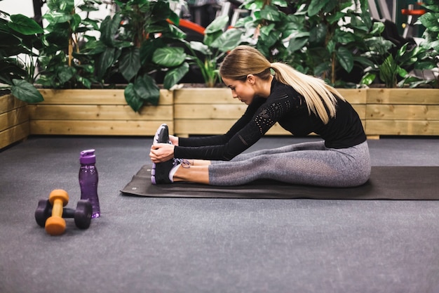 Side view of a young woman stretching her leg in gym