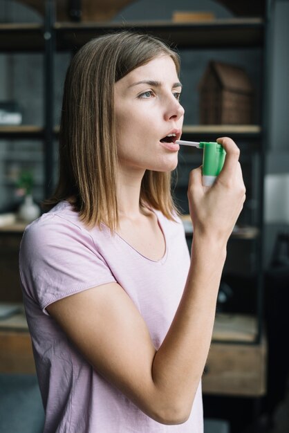 Side view of a young woman using throat spray