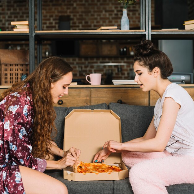 Вид сбоку молодых женщин, принимая ломтики пиццы из коробки