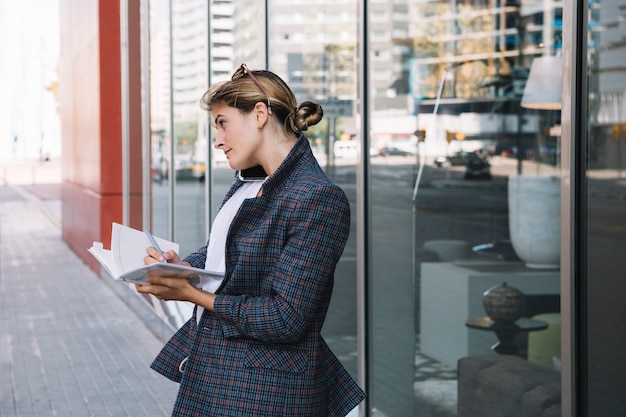 Free photo side young businesswoman writing in the notebook with pen