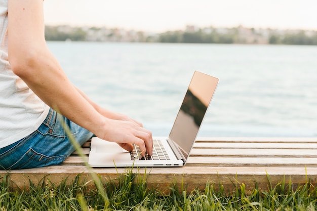 Free photo sideview man using laptop by the water