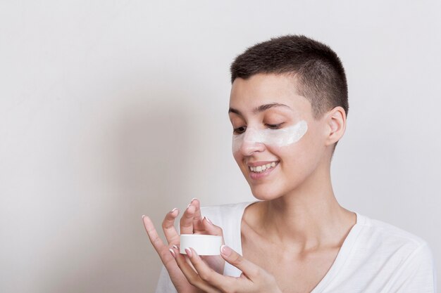 Sideway young woman applying cream on face