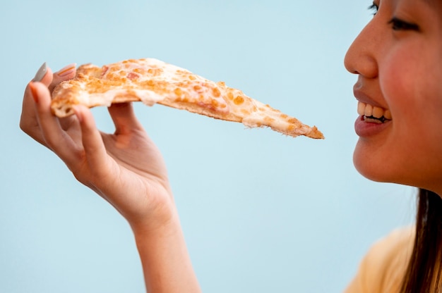 Sideways asian woman eating a slice of pizza