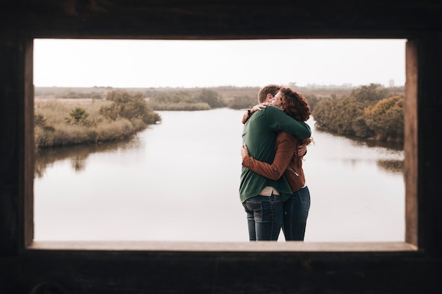 Free photo sideways couple hugging next to a pond