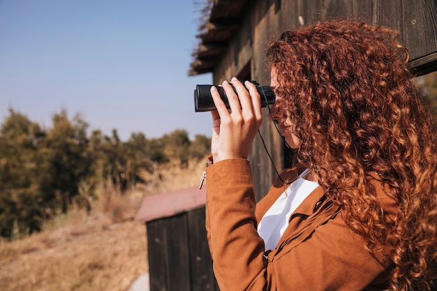 Sideways curly redhead woman watching through binoculars