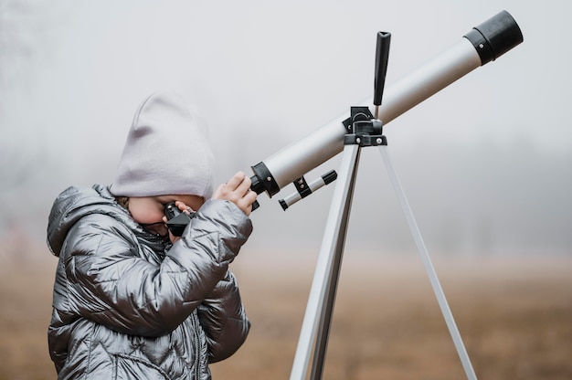 Foto gratuita bambina lateralmente utilizzando un telescopio