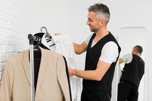 Бесплатное фото Боком мужчина расставляет одежду на вешалках