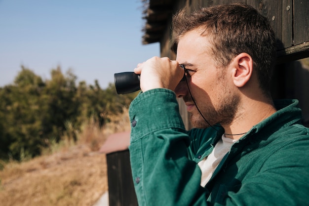 Uomo lateralmente che osserva tramite il binocolo