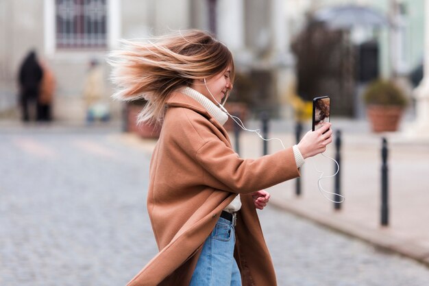 Sideways modern young woman listening to music on earphones