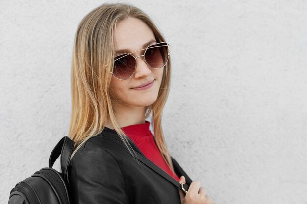 Sideways portrait of stylish teenage girl with fair hair wearing big trendy sunglasses