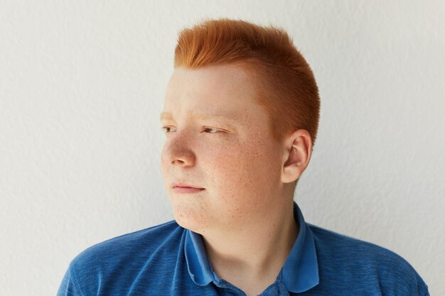 トレンディな髪型とカジュアルなブルーを着ているそばかすのある思慮深い赤毛の男の子の横向きの肖像画