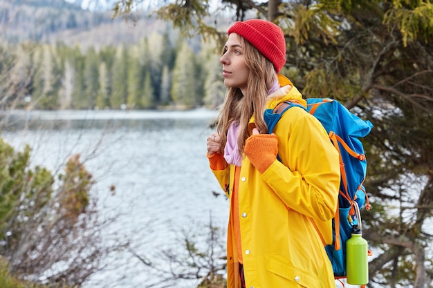 Sideways shot of beautiful female traveler stands with backpack