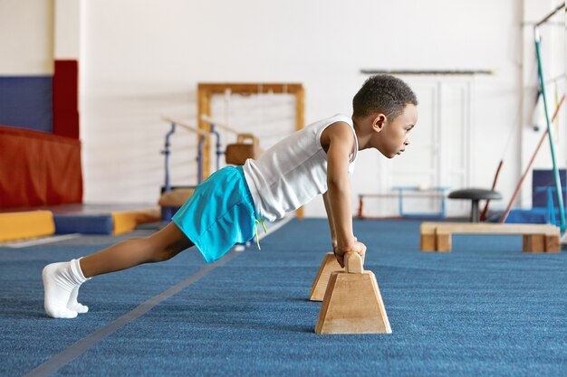 Sideways shot of concentrated serious Afro American kid in sports clothes keeping feet on floor