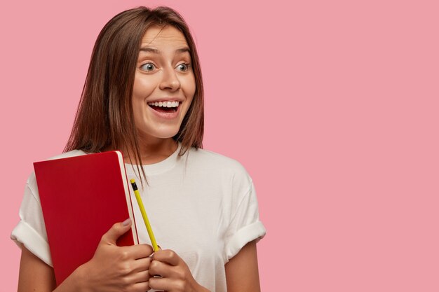 Sideways shot of glad amazed student happy to see groupmate into distance, has toothy smile, carries notebook and pencil