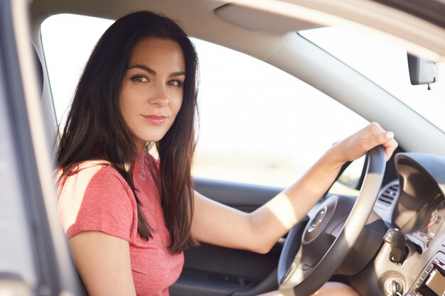 Sideways shot of good looking serious brunette girl drives car professionaly
