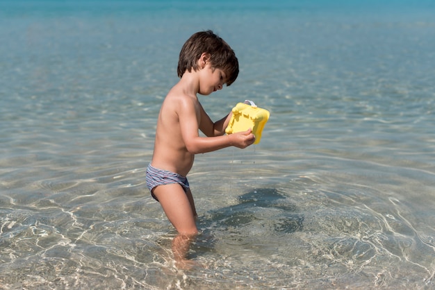 水の中の砂のバケツで遊んでいる子供の横ショット