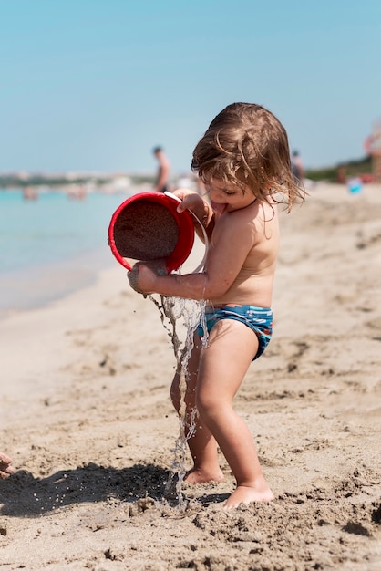 Боковой снимок ребенка, играющего с ведром с песком